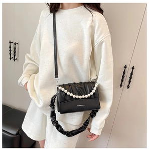 Detail of black pleated crossbody bag with elegant white pearl chain and fashion lettering