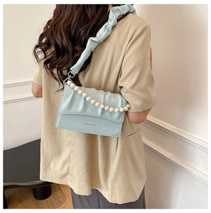 Detail of light blue pleated flap crossbody bag with pearl handle and textile strap