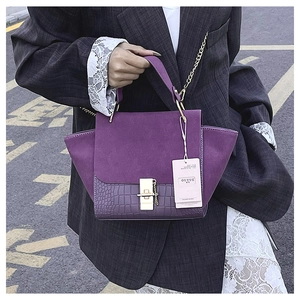 Detail of purple winged bag with matte finish, crocodile texture, and gold hardware