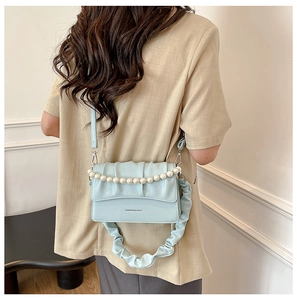 Detail of light blue crossbody bag with ruched strap and decorative pearl chain handle