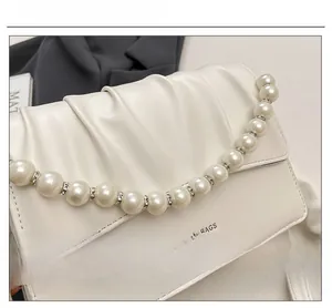 Detail of pleated faux leather texture with pearl and rhinestone trim on the cream handbag