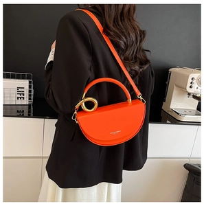 Detail view of orange semi-circular leather handbag with gold ring decoration and shoulder strap
