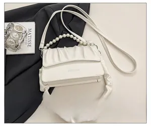 Detail of cream pleated crossbody bag featuring pearl handle and stylish strap accents