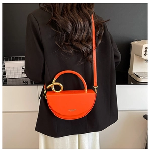 Detail of orange semi-circle crossbody bag with gold metal knot handle and long strap