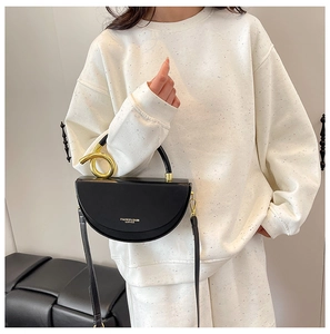 Detail of a black leather crescent bag with an elegant gold-toned knotted metal handle