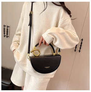 Detailed view of black semi-circular bag featuring unique gold twisted ring handle design