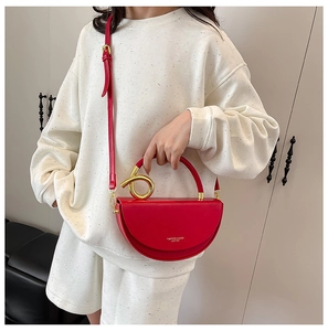 Detail of red semi-circular bag featuring a unique spiral gold handle and logo