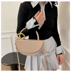 Detail of beige crescent bag with a gold twisted metal handle and matte leather finish