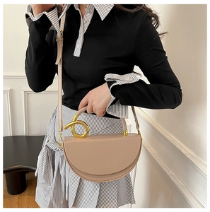 Detail of a beige saddle bag featuring a unique twisted gold metal handle and leather strap