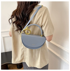 Detail of light blue crescent bag with golden twisted ring hardware and leather strap