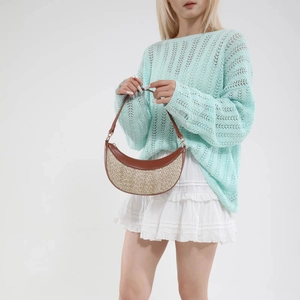 Straw half-moon crossbody bag with brown leather trim worn by model in casual style