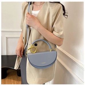 Close-up of fog blue half-moon bag with golden spiral metal handle and leather strap