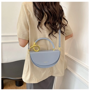 Close-up of light blue crescent bag with golden knot handle and fashion text detail