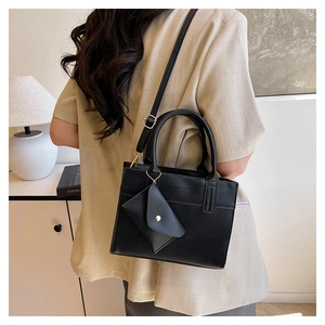 Détail du sac carré en cuir noir avec mini pochette porté par un mannequin femme