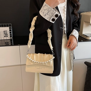 Chic beige crossbody bag with pearl chain detail and pleated strap in a lifestyle setting