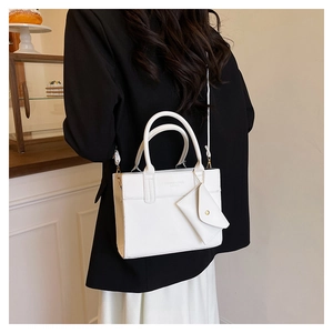 Détail du sac à main blanc avec breloque enveloppe et bouton doré sur un blazer noir