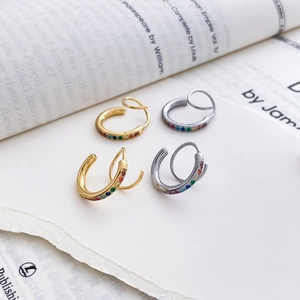 Détail de créoles dorées et argentées serties de strass arc-en-ciel sur pages de livre