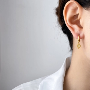 Boucles d'oreilles créoles dorées avec pendentif losange gravé d'une étoile sur mannequin