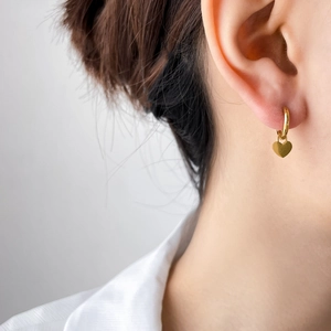 Détail d'une boucle d'oreille créole avec pendentif cœur doré portée par un modèle