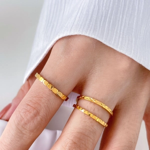 Dettaglio di anelli placcati oro con maglie a catena e texture geometriche sulla mano