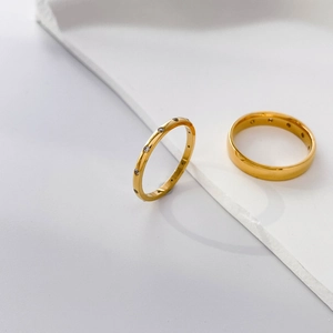 Detail of two gold-plated rings, one with zircons and one minimalist band on marble