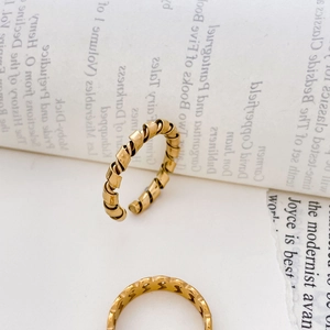 Gros plan sur une bague spirale dorée torsadée et une bague ajourée sur pages de livre