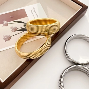 Detailed view of wide gear-textured C-shape stainless steel bracelets in gold and silver