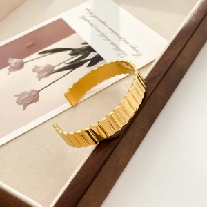 Detail of gold-plated stainless steel cuff with wavy gear texture on a vintage backdrop