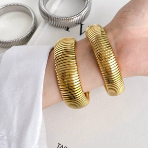 Macro detail of thick industrial gear-textured spring bangles in gold and silver finish