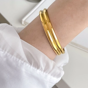 Detailed view of two polished gold-plated stackable round bangles on a model's wrist