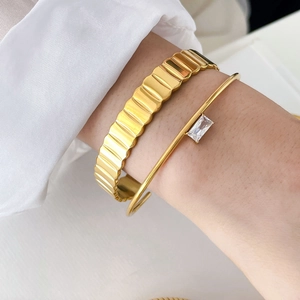 Close-up of a wide scalloped gear-patterned gold bangle with a rectangular zircon C-ring