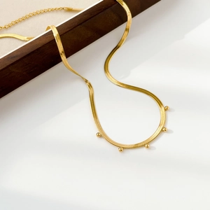 Detail of gold snake chain necklace featuring five small metal beads and lobster clasp