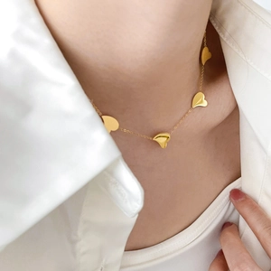 Close-up of minimalist 18K gold snake chain necklace with small 3D heart charms on neck