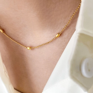 Close-up of golden beaded chain necklace with oval gold bean accents on a white shirt