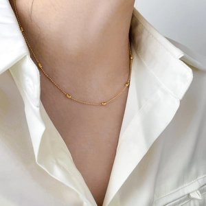 Minimalist gold chain necklace with cylinder metal beads on model with white shirt