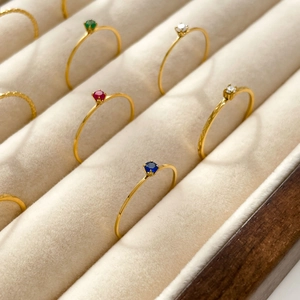 Row of minimalist gold thin rings with colorful round gemstones in a velvet jewelry box