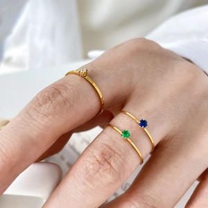 Detail of three dainty gold-plated stackable rings with colorful crystals on a textured band
