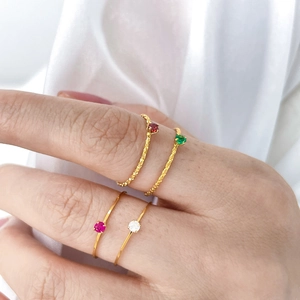 Close-up of four thin gold rings set with colorful red, green, and white gemstones
