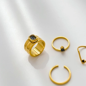 Set of four gold-plated rings featuring black zircon stones on a white background