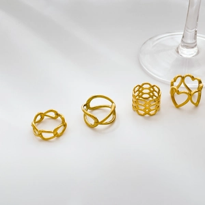Lot de quatre bagues dorées ajourées avec motifs cœur et chaîne sur fond blanc