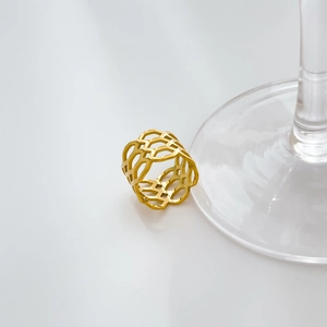 Détail d'une large bague à motif géométrique creux en finition dorée sur socle en verre