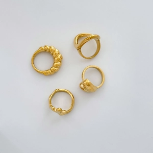 Flat lay of four gold minimalist rings featuring croissant, lava, and hollow designs