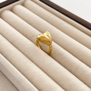 Detailed close-up of a polished gold heart-shaped ring in a beige velvet jewelry box