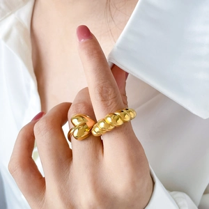 Detail of model wearing a gold heart ring and a twisted rope band with white shirt