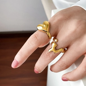 Detail of gold heart and abstract lava fluid rings on a finger with a modern minimalist style