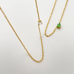 Vue détaillée de fines chaînes dorées avec pendentifs zircons verts et blancs en poire