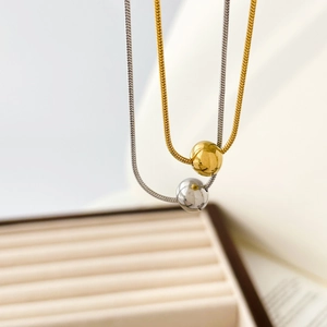 Gros plan de chaînes serpent or et argent avec pendentifs boules lisses suspendus