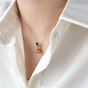 Détail d'un collier pendentif bouteille dorée porté sur une chemise blanche