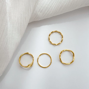 Flat lay of four minimalist gold wavy stackable rings on a clean white fabric background