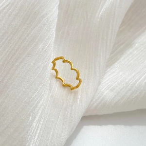 Close-up of a minimalist gold wavy ring on soft white fabric highlighting texture